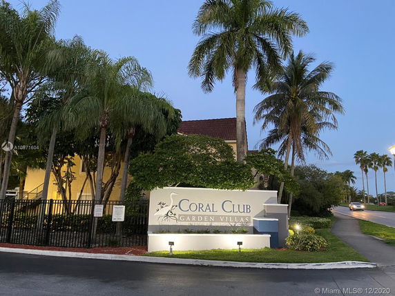 Front view of a building with a garden and the sign 'Coral Club Garden Villas'.