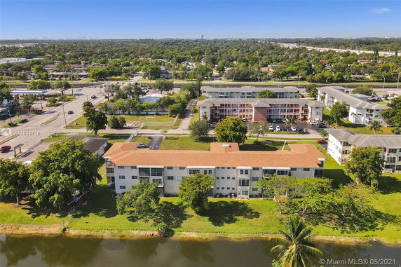 Aerial view of multiple apartment buildings with a pond in the foreground and roads in the background.