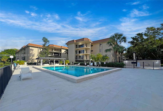 Outdoor swimming pool area in front of a multi-story residential building.