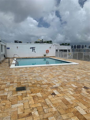 Outdoor swimming pool area with tiled flooring and surrounding safety railing.