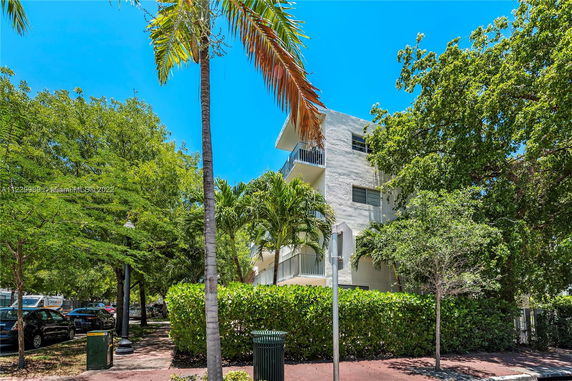 Front view of a multi-story building with balconies surrounded by trees.