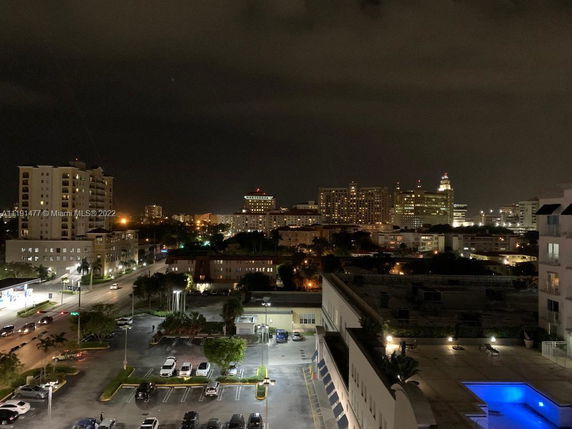 Panoramic view of illuminated buildings at night with a parking lot and a blue-lit pool.