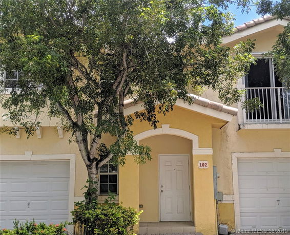 Front view of a two-story house with a yellow exterior, a balcony, and a double garage.