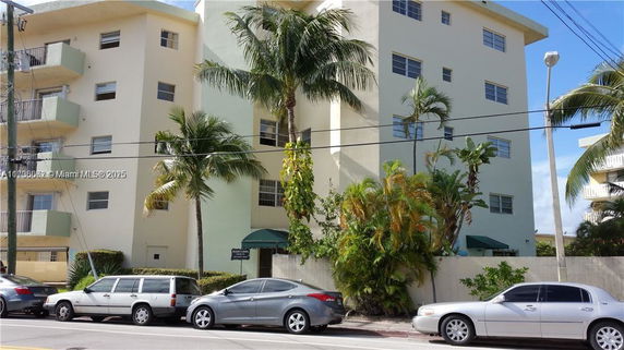 Front view of a multi-story residential building with balconies and palm trees.