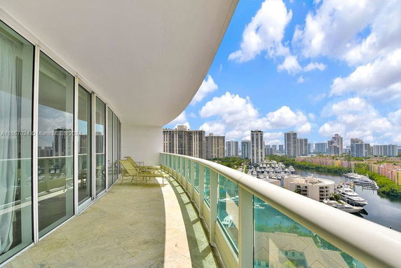 Panoramic view from a curved balcony with glass railings overlooking a cityscape and marina.