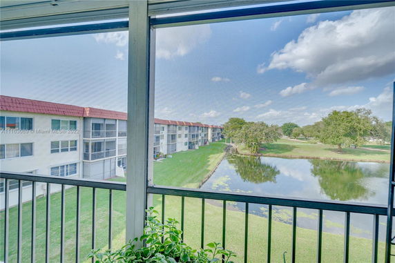 View from a balcony overlooking buildings and a pond with grassy areas and trees.