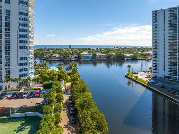 View of waterfront buildings with a river in the foreground and additional structures on the distant shore.