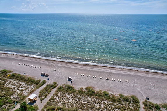 Aerial view of a beach with rows of lounge chairs and the ocean in the background.