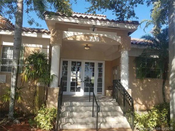 Front view of a building with steps leading to a covered entrance, featuring pillars and a tiled roof.