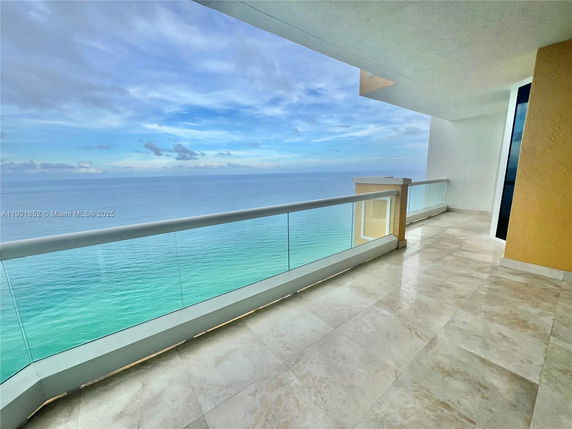 Balcony view overlooking the ocean with glass railing and tiled floor.