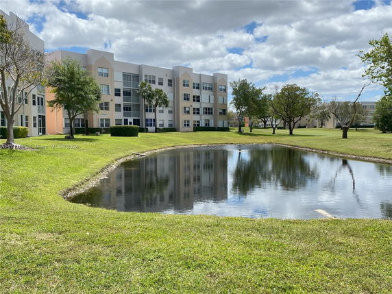 View of a multi-story building with a pond and grassy area in front.