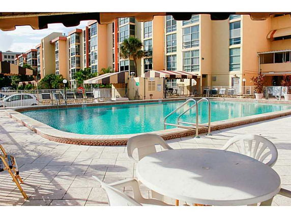 Outdoor swimming pool area with surrounding chairs and tables in front of a multi-story building.