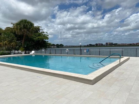 Outdoor swimming pool overlooking a body of water with buildings in the background.
