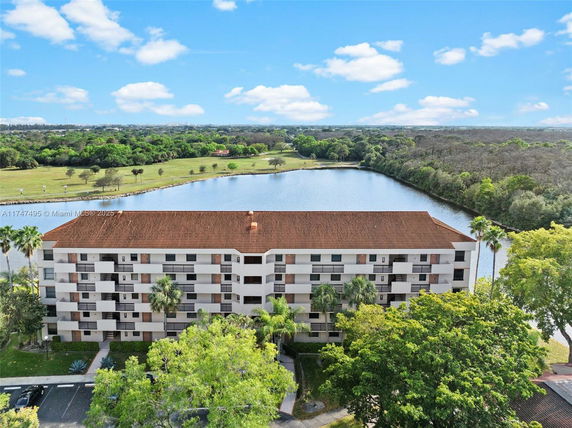 Building with a brown roof surrounded by a wooded area and a body of water.