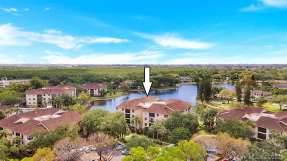 Aerial view of apartment buildings by a lake with surrounding greenery.