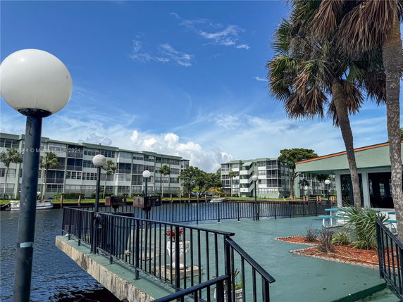 View of multi-story condominium buildings near a water body with railing and palm trees.