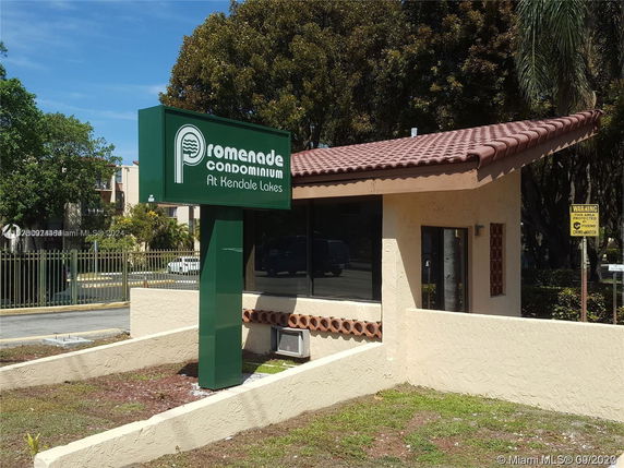Front view of a building with a tiled roof and a sign reading 'Promenade Condominium at Kendale Lakes.'