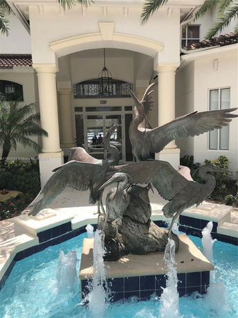 Front view of a building entrance with archway columns and bird sculptures in a fountain.