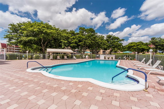 Outdoor swimming pool area with lounge chairs and surrounding trees.