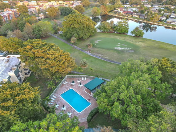 Aerial view of a swimming pool surrounded by trees and adjacent to a golf course and waterbody.
