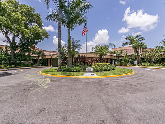 Front view of a building with a tile roof and palm trees lining the entrance.