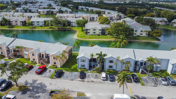 Aerial view of residential buildings by a water body with parked cars and surrounding greenery.