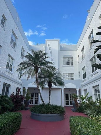 Front view of a multi-story building with white exterior and an entrance surrounded by palm trees.