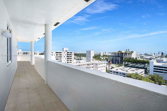Elevated view from a balcony of a cityscape with multiple buildings and a clear sky.