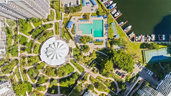 Top-down view of residential complex with a unique round building, pool area, tennis court, parking, and marina.