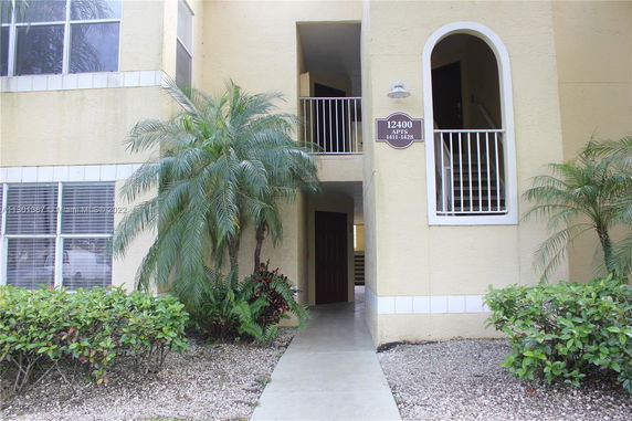 Front view of a multi-story apartment entrance with stairs and railing.