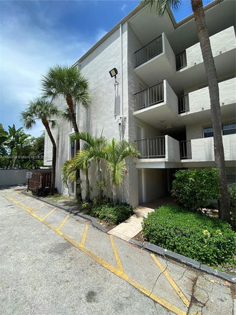 Front view of a multi-story building with balconies and a small garden area.