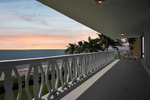 View from a balcony overlooking the ocean and palm trees at sunset.