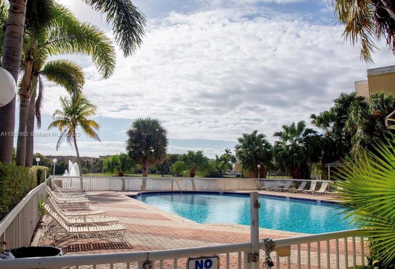 Outdoor swimming pool with surrounding palm trees and lounge chairs.