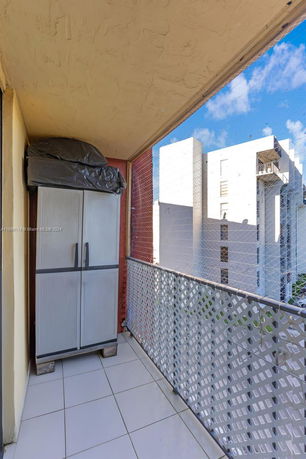 Balcony view with tiled floor and storage cabinet overlooking adjacent buildings.