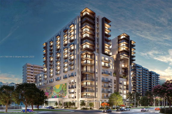 Front view of a multi-story modern apartment building with balconies and illuminated windows.