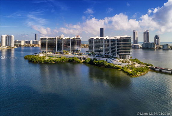 View of modern waterfront buildings on a small island connected by a bridge.