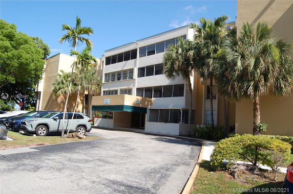 Front view of a multi-story building with a parking area and palm trees.