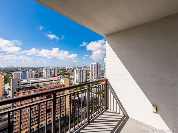 Panoramic view from a balcony overlooking a city with multiple buildings and a clear blue sky.