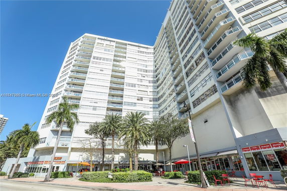 Front view of a tall multi-story building with balconies and commercial spaces at the ground level.