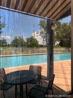 View from behind a glass pane overlooking a swimming pool with a patio area.