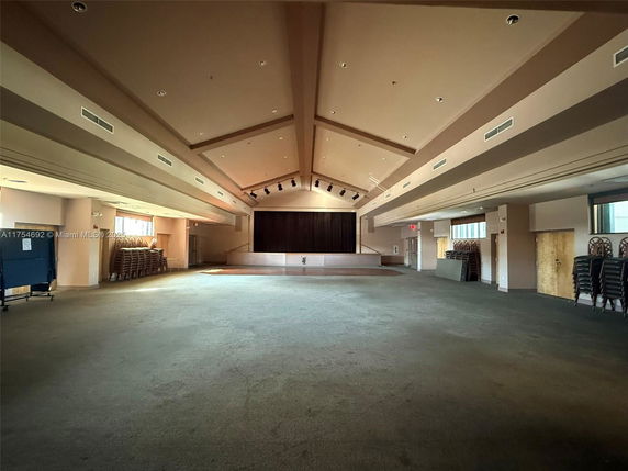 Spacious indoor hall with a stage and stacked chairs.