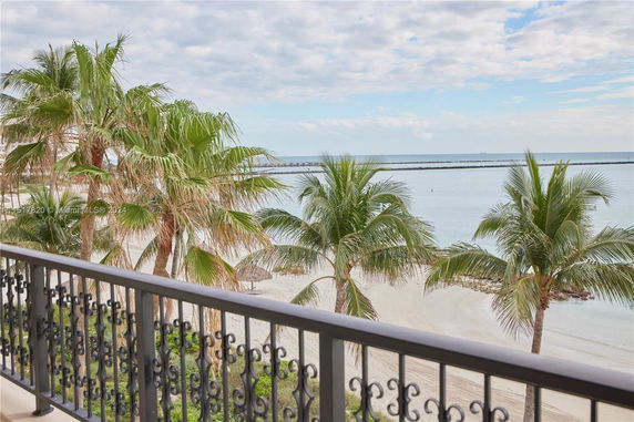 View of a beach with palm trees and the ocean in the background from a balcony.