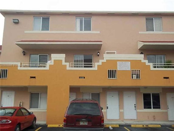 Front view of a three-story building with multiple balconies and parking spaces.