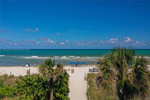 Panoramic view of a beach with blue umbrellas and ocean waves.