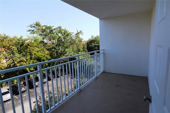Balcony with white railing overlooking a treed area with parked cars below.