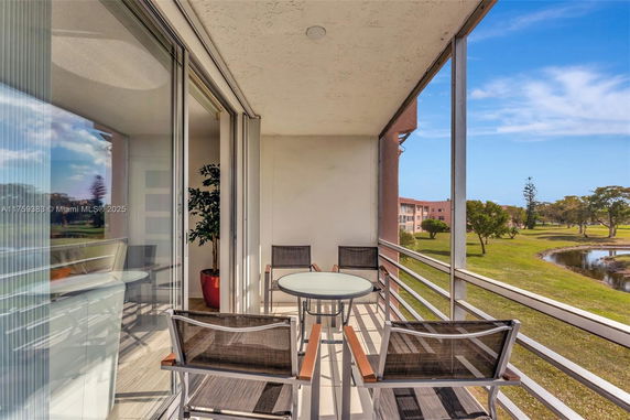 Balcony view with outdoor furniture overlooking green area and pond.