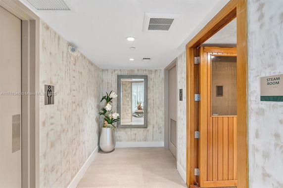 Interior view of an area leading to a steam room with decorative plants and mirror.