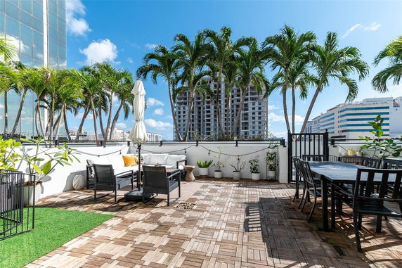 Rooftop terrace with seating, dining area, plants, and view of palm trees and buildings.