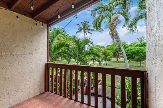 View from a balcony with wooden railing overlooking a garden with palm trees.