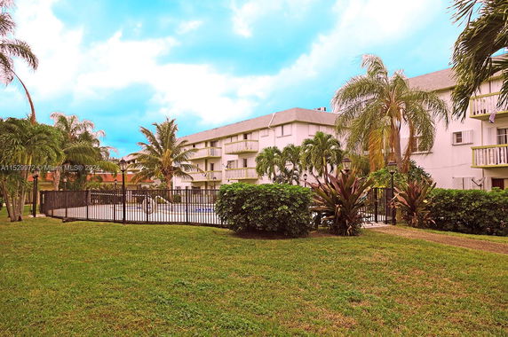 Outdoor swimming pool area surrounded by a fence, adjacent to a multi-story building.